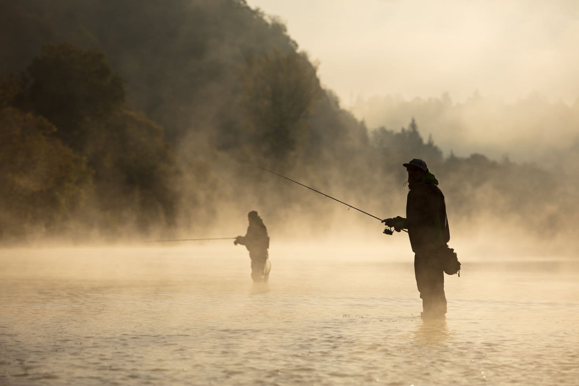 Two anglers wading a misty river at dawn